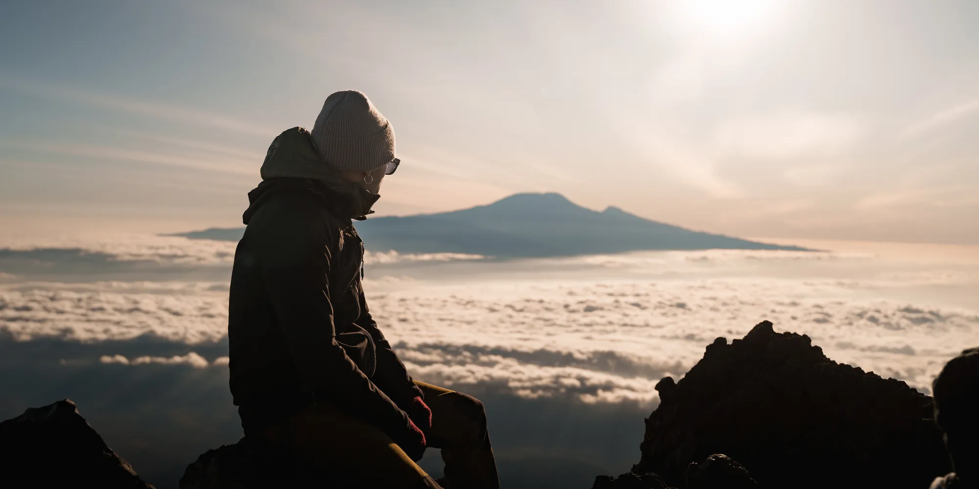 Senderista en la cumbre del Monte Meru al amanecer con el Kilimanjaro al fondo