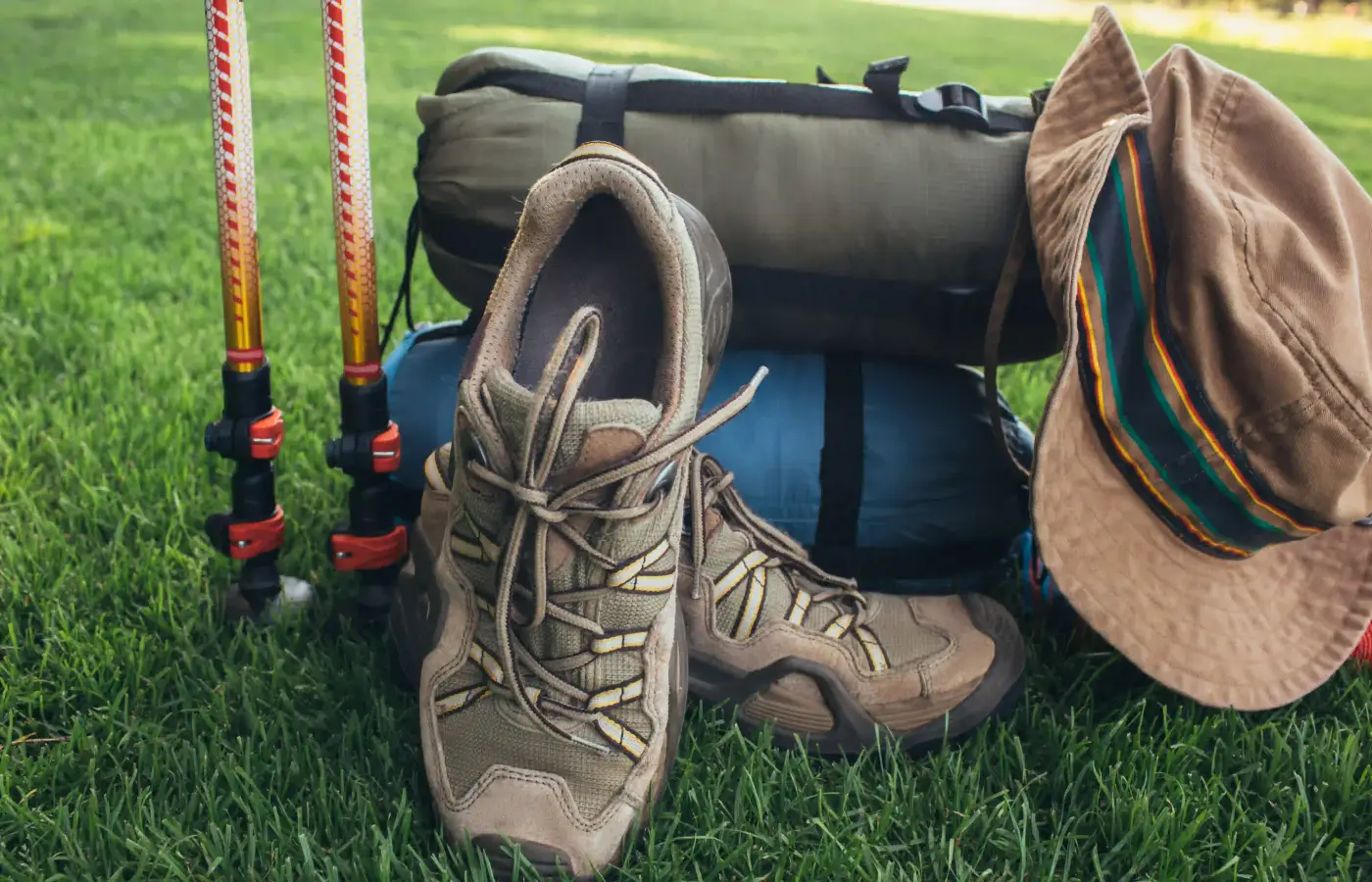 Wanderschuhe, Trekkingstöcke, aufgerollte Matten und ein Buschhut im Gras