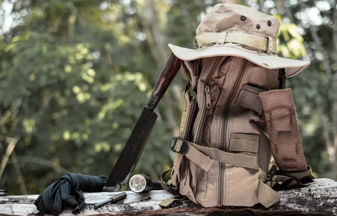 Ein Tagesrucksack mit Buschhut, Taschenlampe und Messer auf einem Baumstamm