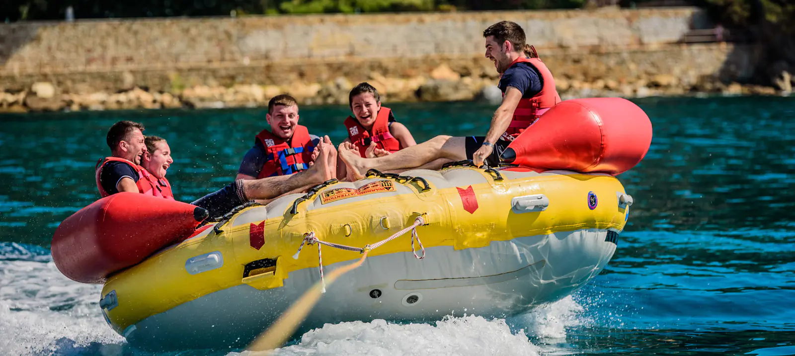 Travellers in life jackets riding an inflatable towed across the sea