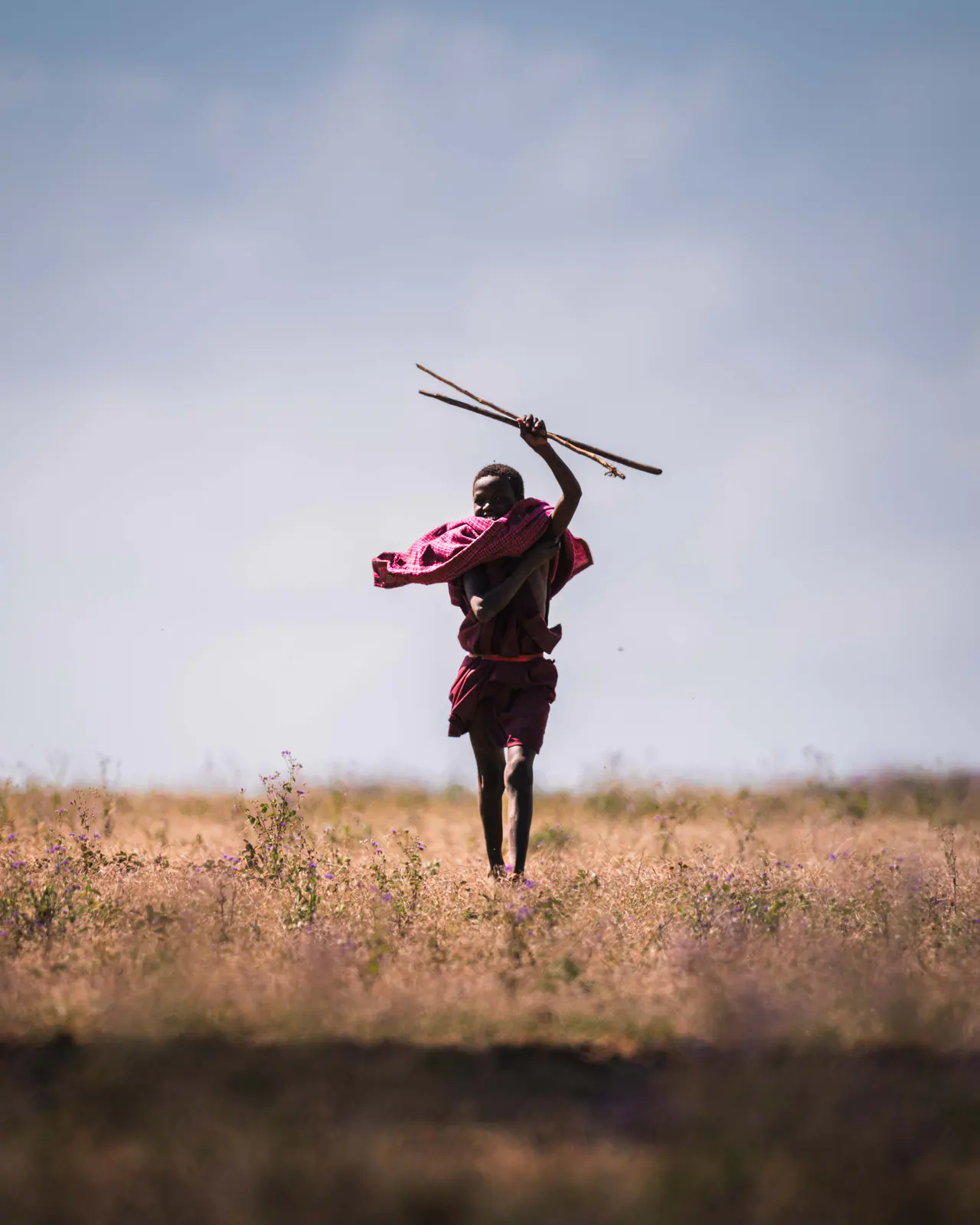 A Maasai warrior in a red shuka crossing open grassland