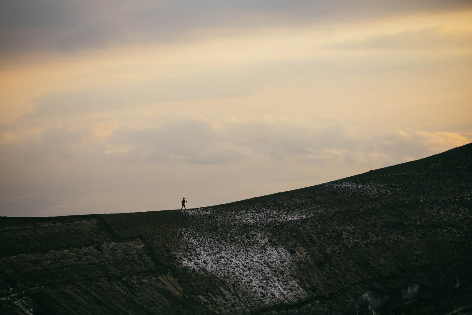 A lone figure walking a volcanic ridge
