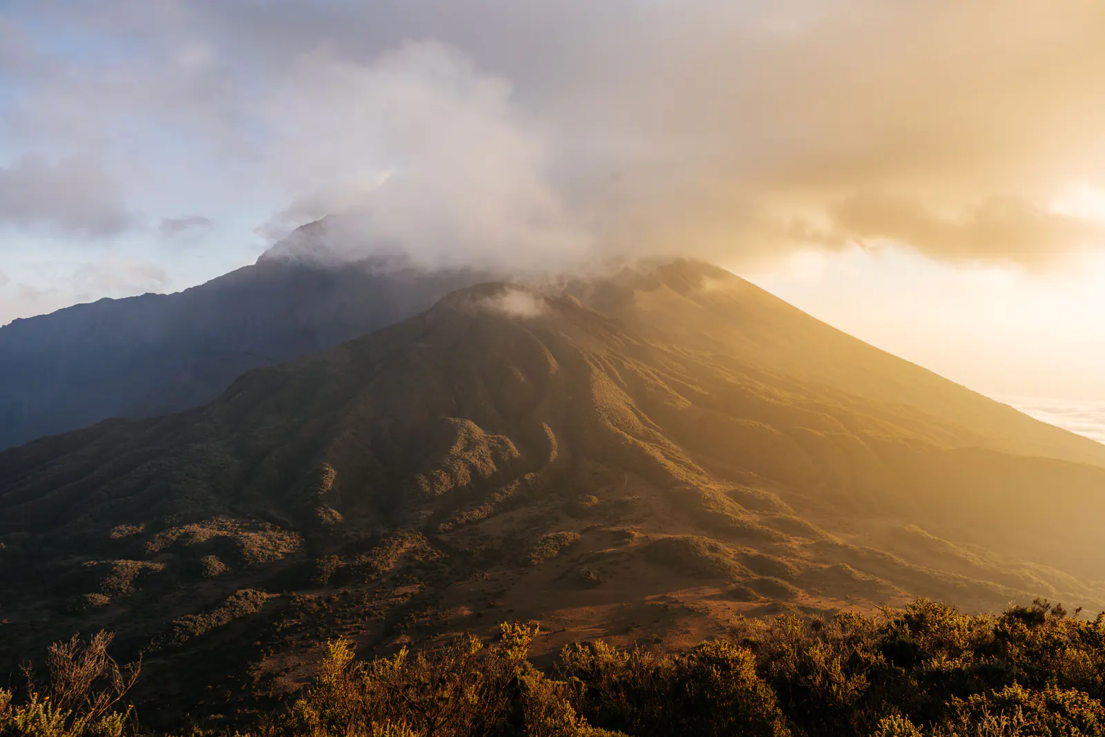 Golden light over a volcanic summit above the clouds