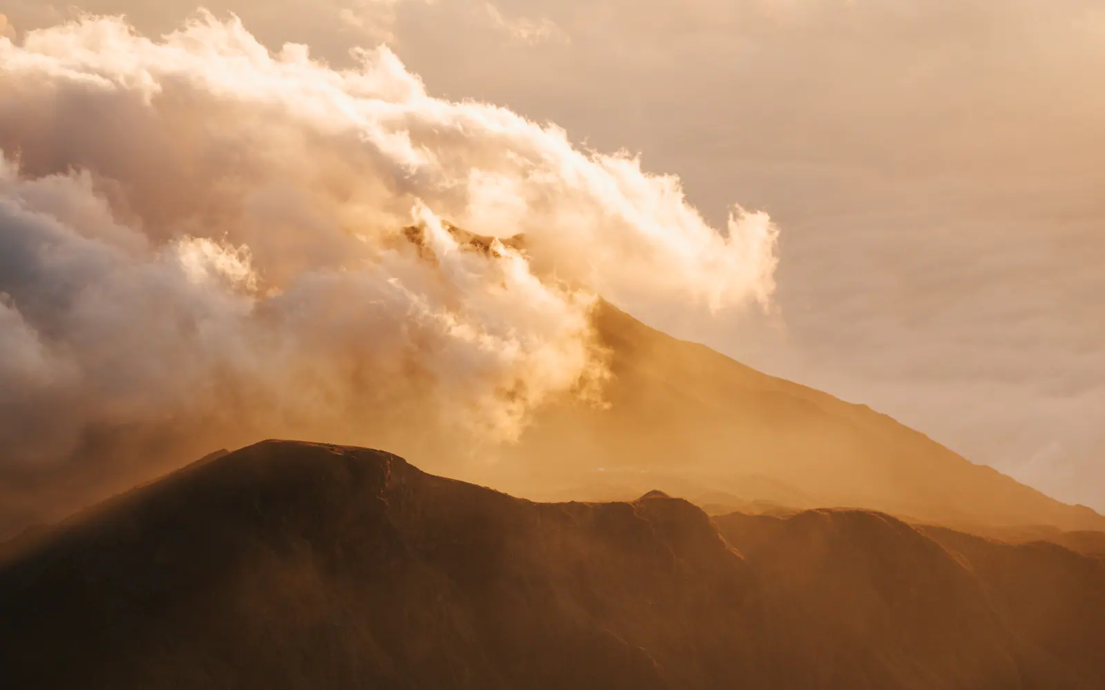 Golden light over a volcanic summit above the clouds