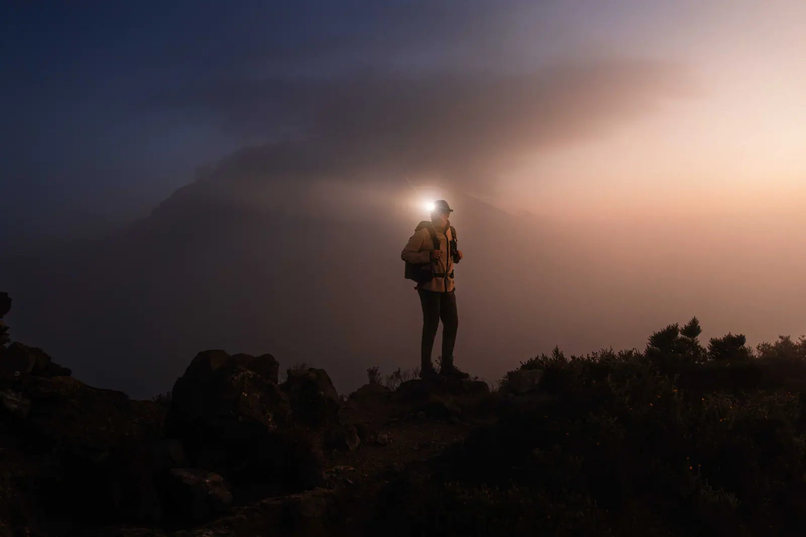A trekker with a headlamp on the pre-dawn climb