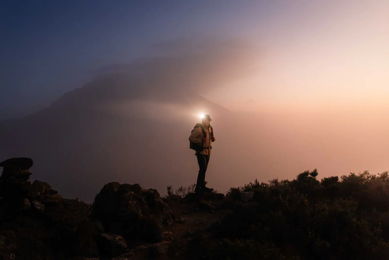 A trekker with a headlamp on the pre-dawn climb